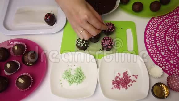 一个女人用洒满巧克力球装饰做一个土豆蛋糕盘子旁边有蛋糕液体巧克力和视频的预览图