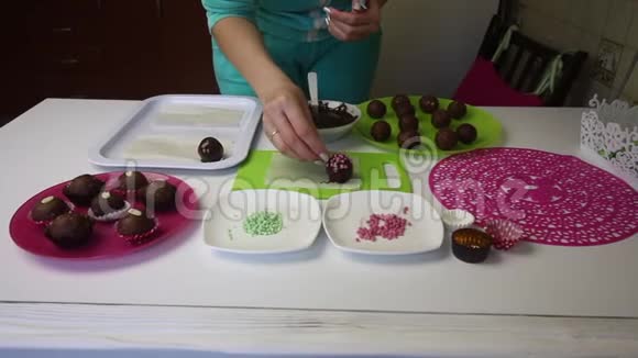 一个女人把巧克力球洒在海绵蛋糕上做一个土豆蛋糕盘子旁边有蛋糕液体巧克力和视频的预览图