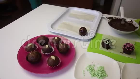 一个女人把巧克力球洒在海绵蛋糕上做一个土豆蛋糕盘子旁边有蛋糕液体巧克力和视频的预览图