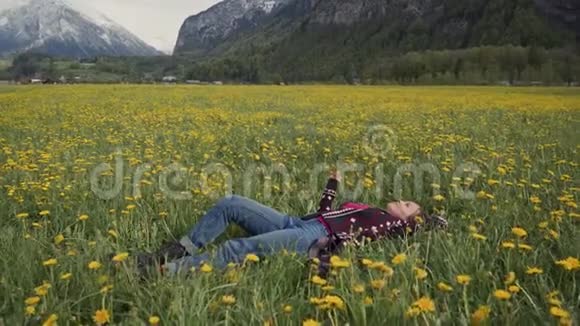 年轻漂亮的女人在田野里用蒲公英的花放松侧视图视频的预览图