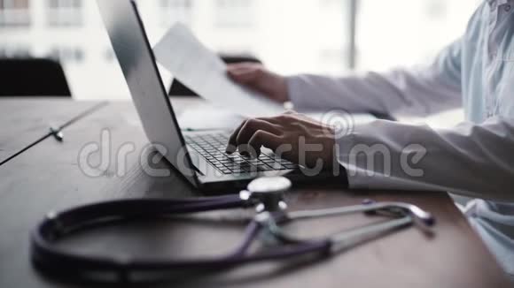 穿着白色外套的医生正在笔记本电脑上打字靠在大窗户上特写视频的预览图