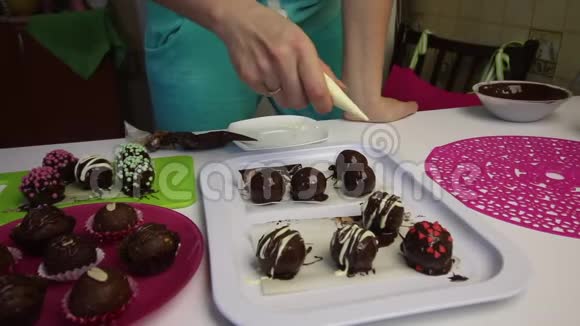 一个女人在巧克力中装饰不同的巧克力球和饼干浆做土豆蛋糕在盘子旁边视频的预览图