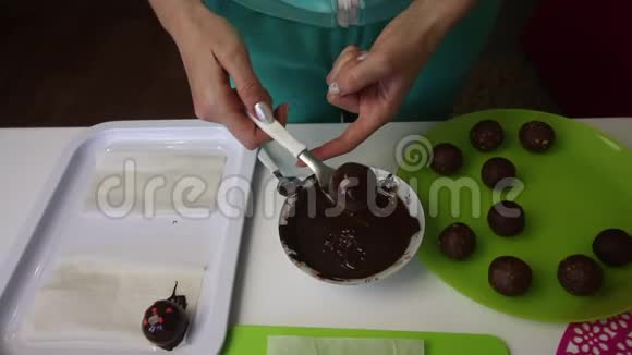 一个女人把一个巧克力海绵球放在表面做一个土豆蛋糕盘子旁边有蛋糕液体巧克力和视频的预览图