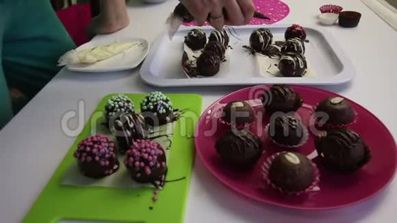 一个女人在巧克力中装饰不同的巧克力球和饼干浆做土豆蛋糕在盘子旁边视频的预览图