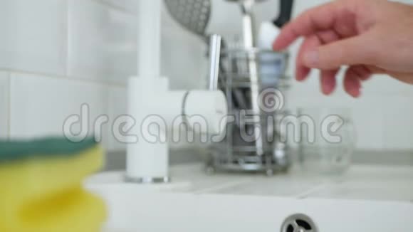 长者手打开自来水在厨房水槽中冲洗一个浸湿海绵视频的预览图