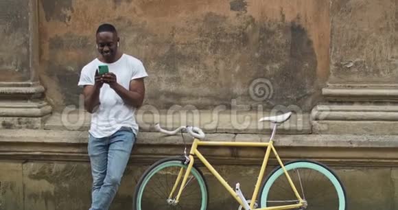快乐微笑的美国男人在耳机使用他的智能手机在社交网络中键入信息男运动员视频的预览图