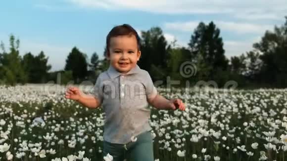 一个小男孩跑过一片花草地微笑着视频的预览图
