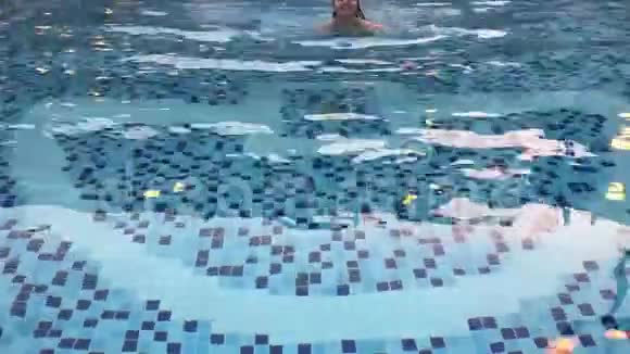 漂亮的白种人年轻女子在泳池里游泳对着镜头游泳微笑视频的预览图