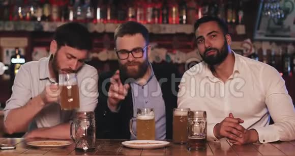 三个老朋友喝啤酒在体育酒吧聊天足球迷们笑着用啤酒讨论新闻视频的预览图