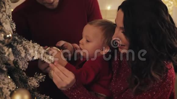 快乐的年轻家庭与小男孩装饰圣诞树在他们明亮舒适的客厅看着幸福的微笑视频的预览图
