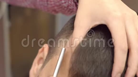 理发师用锋利剃刀把头发剃在人的太阳穴上发型师双手特写视频的预览图