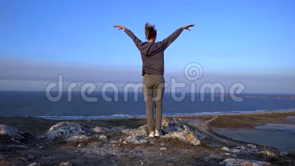 一个身材苗条的女人站在一座高山上迎风招展描绘着她张开双臂飞翔的情景视频的预览图