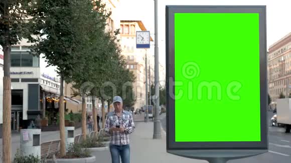 在一条城市街道上一个男人点击广告牌附近的智能手机站视频的预览图
