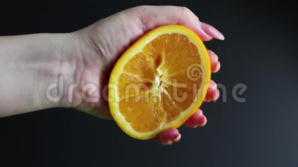 一只雌性的手捏着一半新鲜多汁的橘子柑橘橙汁从橙浆中滴在黑色背景上这就是视频的预览图