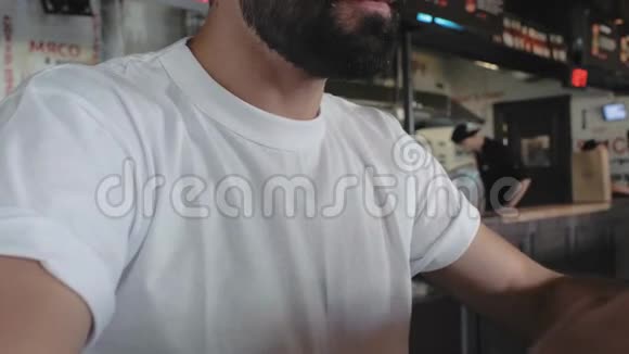 一个穿着白色T恤的家伙咬了一个汉堡鸭子和番茄酱把他滴在白色T恤上男人吃汉堡包4k4k录像视频的预览图