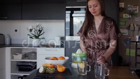 一位年轻女子在厨房的杯子里倒着一个榨汁机刚做的橙汁视频的预览图
