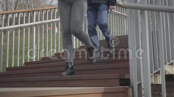 无法辨认的女孩和男孩走在木楼梯上离开阳光明媚的一天男人和女人的腿在公园里散步视频的预览图