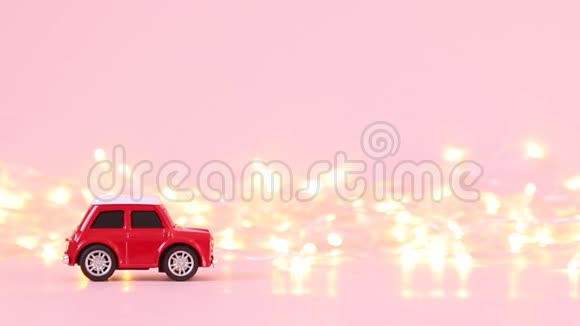 红色儿童玩具车和粉红色背景上的金色闪烁花环假日概念视频的预览图