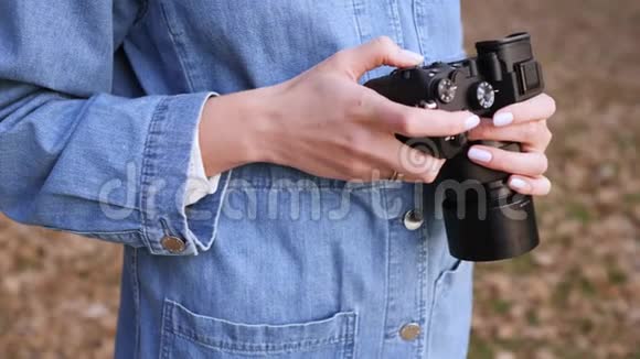 黑色相机在女性手中特写一个穿牛仔衣服的女人看着镜子里的镜头选择镜头视频的预览图