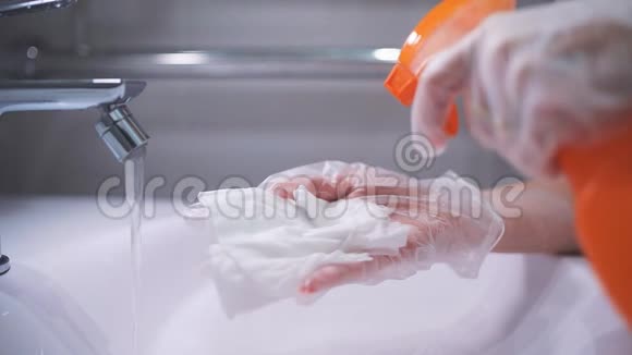 戴手套的女人清洗浴室的水龙头和水槽在抹布上喷洒泡沫每天清洗和消毒视频的预览图