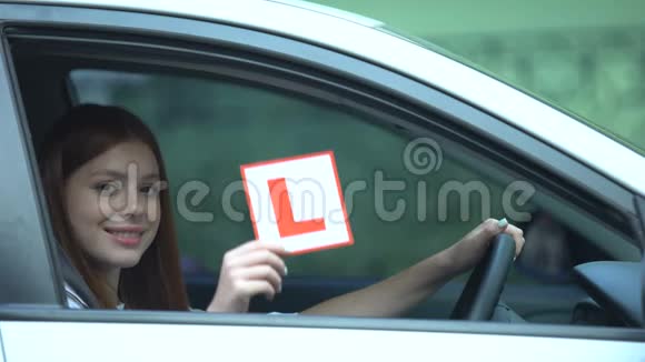 微笑的女孩在车窗上驾驶课程左撇子的交通中显示l板视频的预览图