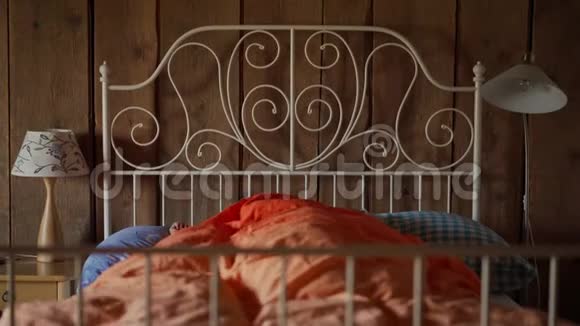 美丽的年轻女子在一张白色的锻铁床上醒来床上有彩色的床上用品视频的预览图