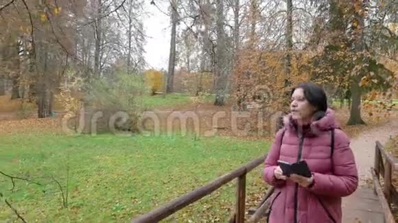 秋天公园白种人中年妇女在智能手机上拍摄自然视频的预览图