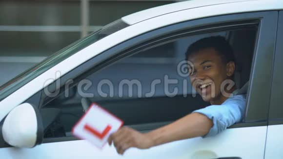 微笑的男孩在车窗上展示l板驾驶课程右手交通视频的预览图