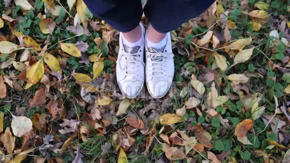 女人脚穿白色时尚运动鞋在美丽的落叶上从上面看秋天树叶覆盖视频的预览图