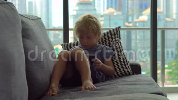 小男孩用平板电脑坐在一扇大窗户前背景是摩天大楼他有麻烦了视频的预览图