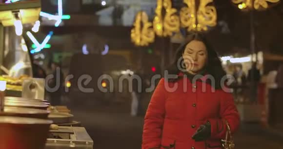 一幅自信的白种人女人穿着红色外套晚上沿着城市市场走来走去环顾四周积极正面视频的预览图