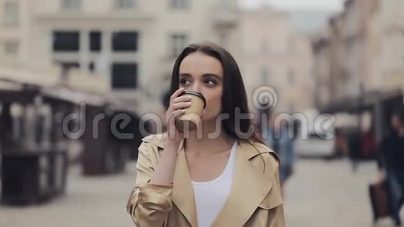迷人的年轻女孩饮酒咖啡站着看镜头和变焦在旧城背景视频的预览图