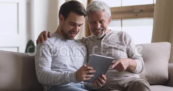 快乐的大爸爸和大儿子在家里使用平板电脑视频的预览图
