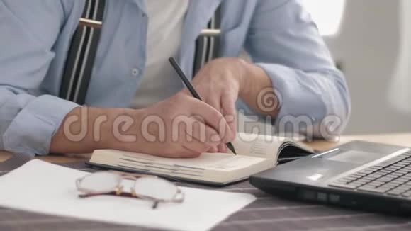 男性在坐在桌子旁的时候双手特写在笔记本上做笔记视频的预览图