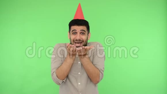 快乐的黑发男人头上戴着派对锥穿着衬衫从他的手掌里吹出纸屑绿色背景色度键视频的预览图
