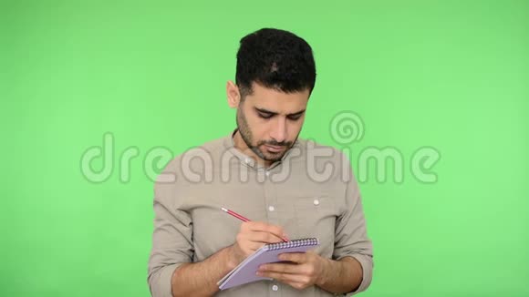 男作家黑发鬃毛穿着衬衫站着在纸笔记本上做笔记绿色背景色度键视频的预览图