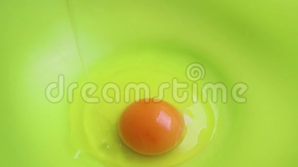 生鸡蛋落入绿色塑料碗中慢动作特写一个鸡蛋已经在那里了做煎饼的过程A视频的预览图