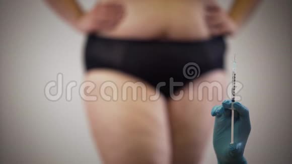 戴着医用手套的女性手拿着注射器站在背景下可辨认的穿着内衣的肥胖女性视频的预览图