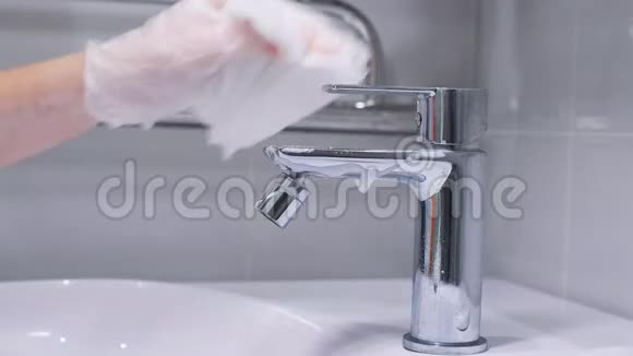 女人戴手套的手用洗涤剂清洗浴室里的不锈钢水龙头检疫卫生Covid19视频的预览图