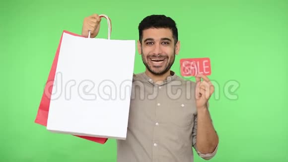 出售高兴兴奋的男性买家穿着衬衫拿着购物袋和销售词说是的摄影棚绿色背景视频的预览图