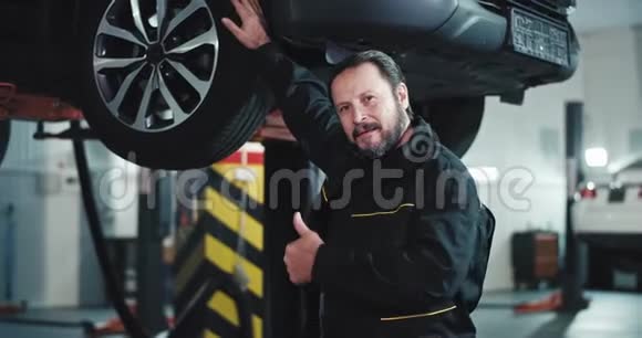 有魅力的成熟的汽车机械师身着制服站在镜头前表现出巨大的喜欢同时站在一辆汽车旁边视频的预览图