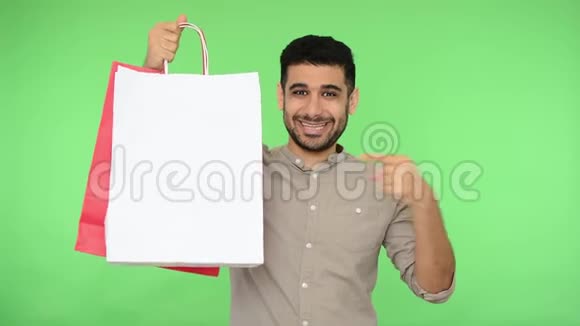 快乐满意的男买家穿着衬衫手指着手中的购物袋竖起大拇指绿色背景视频的预览图