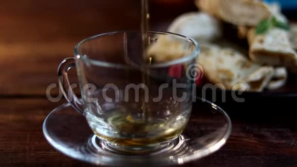 早餐有煎饼和茶把热茶倒进一个透明的杯子里在木制背景上视频的预览图