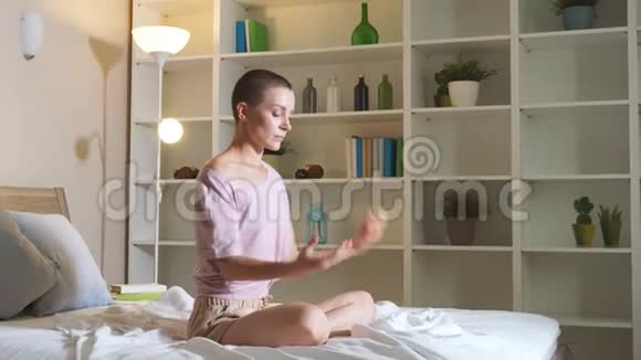 年轻女子正在家里练习瑜伽以简单的身体姿势坐在床上放松视频的预览图
