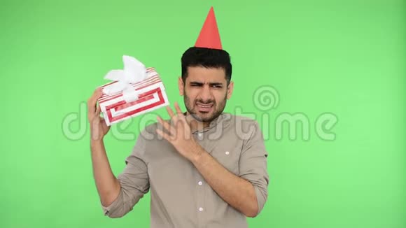 好奇快乐的黑发男人头上戴着派对锥穿着衬衫摇着礼盒绿色背景色度键视频的预览图