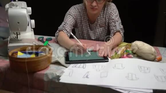 女服装设计师在桌旁的工作室里用数码平板画草图视频的预览图