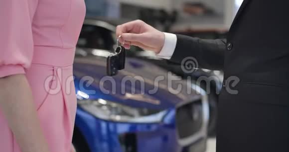 特写镜头一个面目全非的汽车经销商穿着西装把钥匙交给一个穿着粉红色连衣裙的白人女性客户并握着她的手视频的预览图