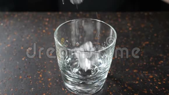 在黑暗的酒吧柜台上用杯中的冰块倒入空的透明玻璃杯中用于威士忌白兰地或波旁酒缓慢视频的预览图