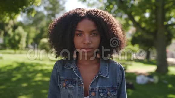 一位非洲裔美国青年妇女站在公园里看镜头的肖像上面有严肃的表情视频的预览图