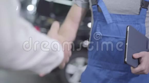 两个面目全非的白种人站在汽车修理店里他们手里拿着相机汽车技工和客户视频的预览图